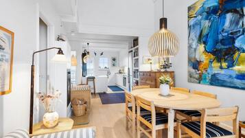 Et moderne køkken med hvide skabe, et spiseområde med et træbord og stole, samt et stort abstrakt billede på væggen.
