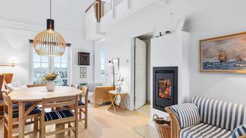 A spacious living room with a high ceiling, a dining area with wooden furniture, and a cozy seating area with a striped sofa.