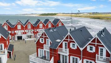 A row of red and white buildings with balconies overlooking a beach and ocean.