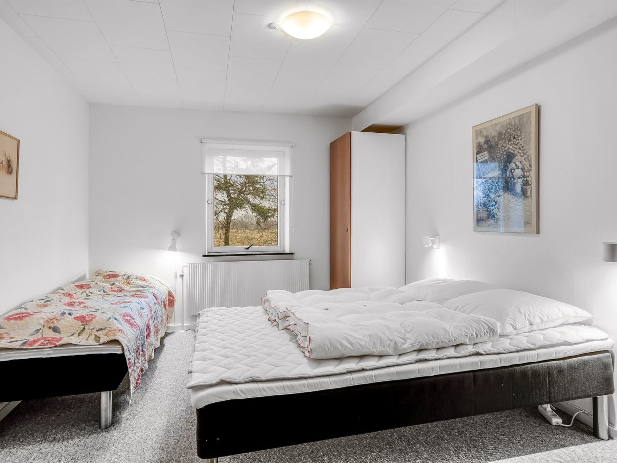 Une chambre à coucher avec un lit, un petit lit, une fenêtre, un radiateur et un tableau accroché au mur.