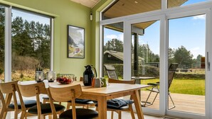 Un comedor con una mesa y sillas de madera, un cuadro en la pared, y vistas a un jardín y edificios exteriores.