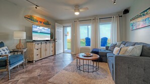 Una sala de estar con sofá, televisor, mesa de centro y vistas al exterior.
