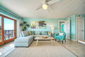 A living room with a sectional sofa, a coffee table, a teal armchair, and a large window with a view.
