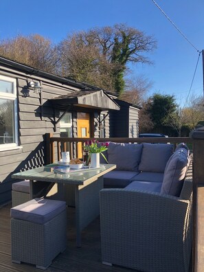 A covered outdoor seating area with a glass table, wicker furniture, and a small garden table with flowers. - Bridge House - Family hideaway by Pett Level Beach, dog friendly! (Hastings)