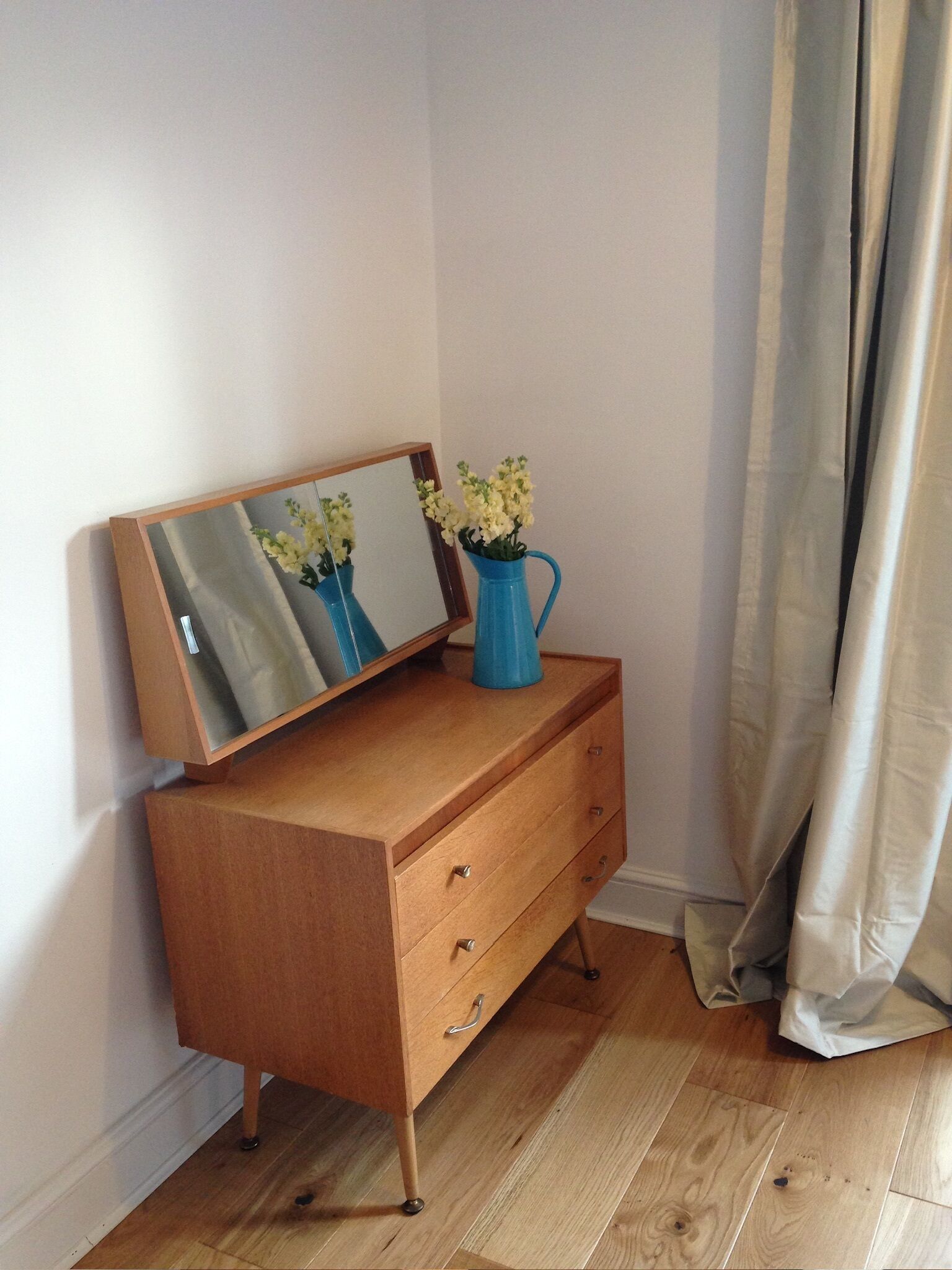 A wooden dresser with a mirror and a vase of flowers.