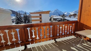 Een balkon met houten hekwerk, een tafel en uitzicht op besneeuwde bergen en gebouwen.