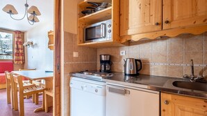 Une cuisine compacte dotée de meubles en bois, d’un four à micro-ondes encastré, d’une machine à café et d’un lave-vaisselle.