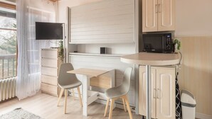 A compact kitchen with a microwave, a small table, two chairs, and a TV mounted on the wall. - Ski-Side Stay in Orcières (Orcières)