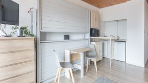 A modern kitchen with a wooden ceiling, white cabinetry, and a small dining area with two chairs and a table. - Ski-Side Stay in Orcières (Orcières)