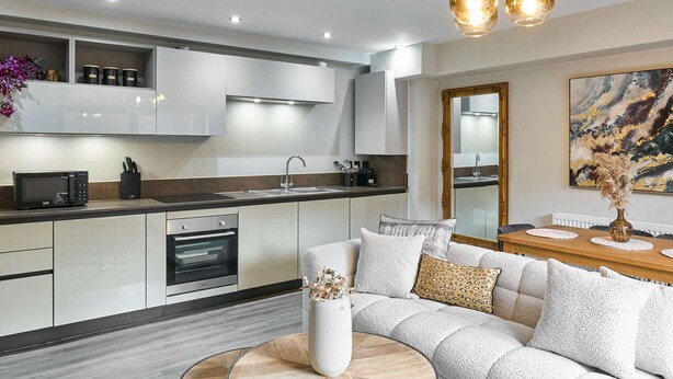A modern kitchen with white cabinets, a microwave, and an oven. There is a dining area with a white sofa and a round coffee table. - Host Stay Chic Townhouse by the Docks (Liverpool)