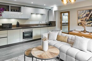 A modern kitchen with white cabinets, a microwave, and an oven. There is a dining area with a white sofa and a round coffee table. - Host Stay Chic Townhouse by the Docks (Liverpool)