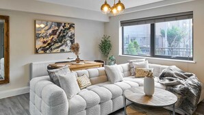 A modern living room with a sectional sofa, a round coffee table, and a large window with a view of the city. - Host Stay Chic Townhouse by the Docks (Liverpool)
