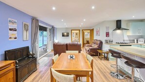 A modern kitchen with a wooden dining table, bar stools, and a built-in oven. - Host Stay Dovecote View (Norwich)