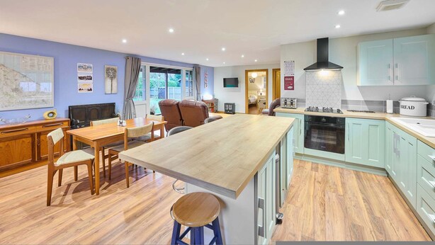 A modern kitchen with a wooden island, light-colored cabinets, and a built-in oven. - Host Stay Dovecote View (Norwich)