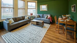A living room with a grey sofa, a wooden coffee table, and a dining table set with chairs. - Host Stay Apartment 1 St Stephens Court (Worcester)