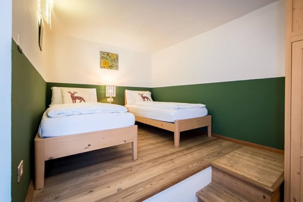 Une chambre avec deux lits en bois, des murs verts et une armoire en bois.