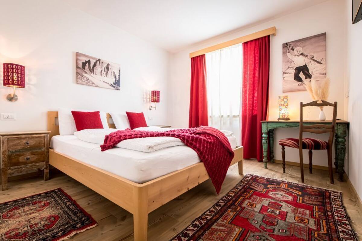 Une chambre à coucher avec un lit en bois, des rideaux rouges, un bureau avec une chaise et un tapis.