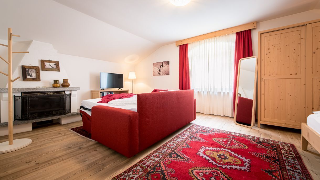 Ein Zimmer mit einem Bett, einem Fernseher, einem Kamin, einem roten Sofa und einem Holzschrank.