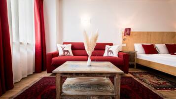A room with a red sofa, a wooden coffee table, a bed with white bedding, and a red and white patterned rug.