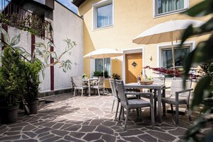 Un patio al aire libre con suelo de piedra, mobiliario de mimbre y plantas en macetas.