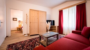 Un salón con un sofá rojo, una mesa de centro de madera, un televisor y un armario.