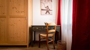 Una habitación con un armario de madera, un escritorio con silla, un cuadro en la pared, una cortina roja y una cesta de mimbre.