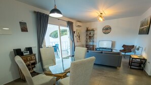 Una sala de estar moderna con una mesa de comedor de cristal, sillas cómodas, un sofá y un televisor.