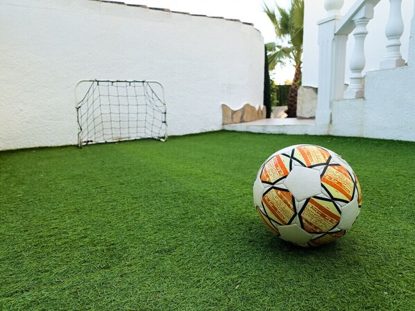 A soccer ball on artificial grass with a white wall and a goal in the background.