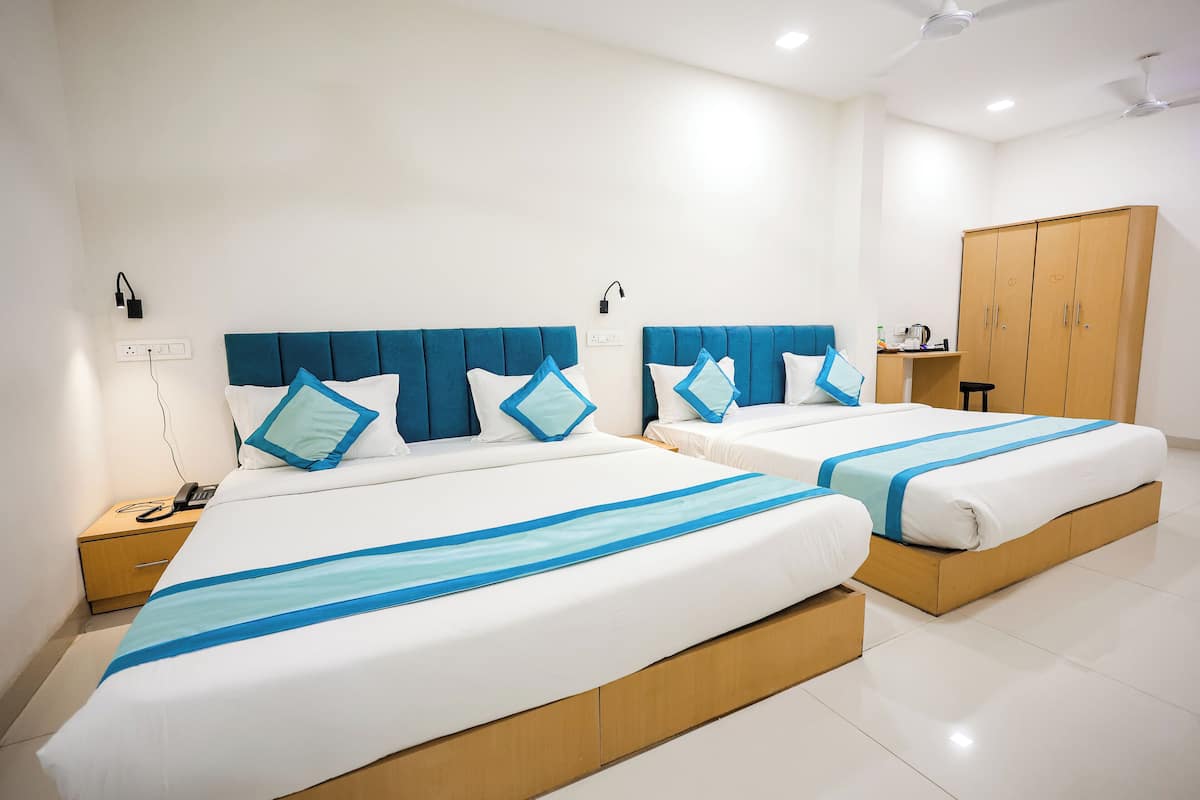 A hotel room with two beds, each with a blue headboard and matching pillows, a wooden wardrobe, and a bedside table with a phone.