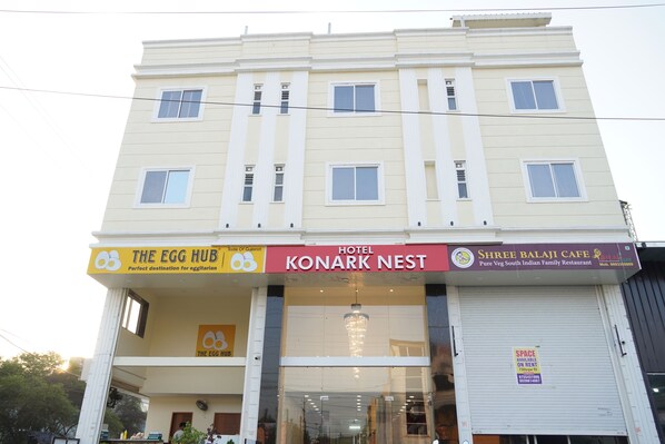 Un edificio de varios pisos con letreros que indican 'The Egg Hub', 'Konark Nest Hotel' y 'Shree Balaji Cafe'.