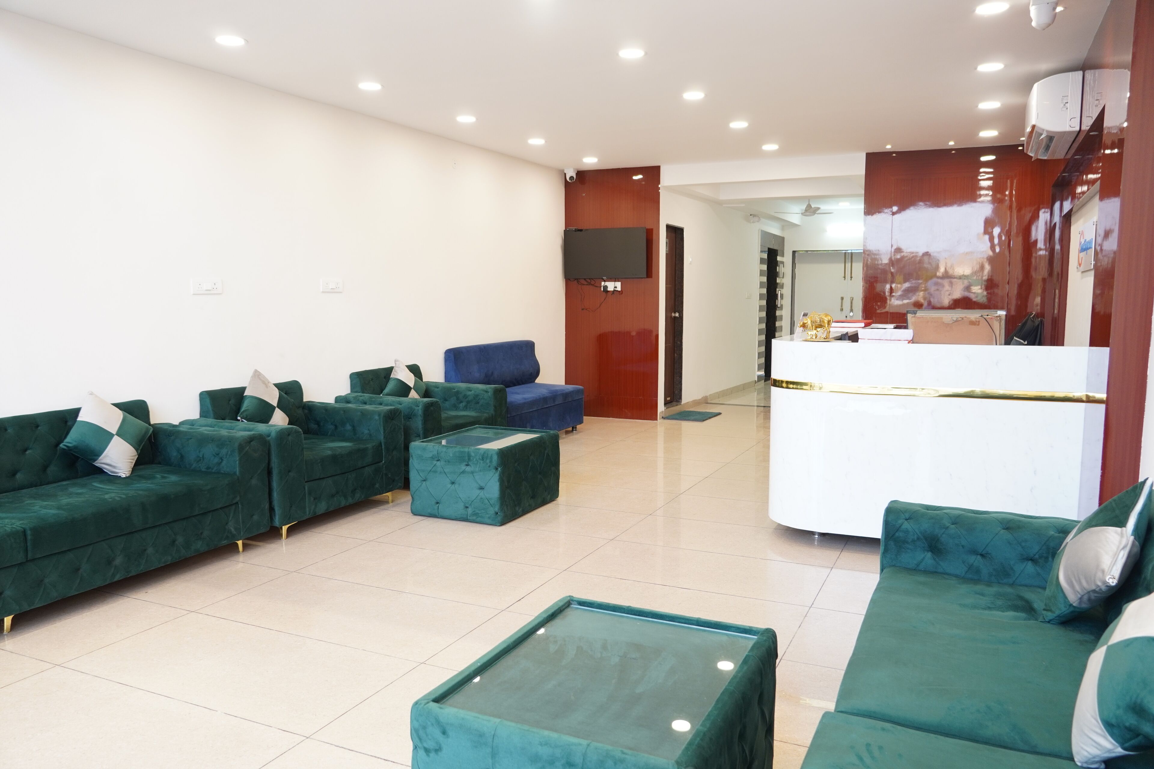 Un moderno vestíbulo de hotel con sofás verdes, un mostrador de recepción y un televisor grande montado en la pared.