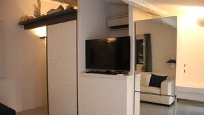A modern living room with a flat-screen TV on a white cabinet, a sofa, and a mirror reflecting the room. - Portofino's Cozy Terrace Wi-fi A/C (Portofino)