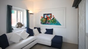 A modern living room with a white sectional sofa, a painting of flowers, and a window with curtains. - Portofino's Cozy Terrace Wi-fi A/C (Portofino)