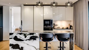 A modern kitchen with a marble island, black bar stools, and pendant lighting.