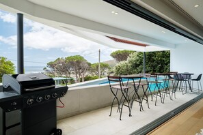 An outdoor patio with a barbecue grill, poolside chairs, and a table. - 4BR Camps Bay Villa w Pool and Garden Casa Meya (Cape Town)