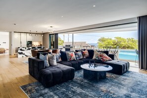 A modern living room with a sectional sofa, a coffee table, and a view of a swimming pool. - 4BR Camps Bay Villa w Pool and Garden Casa Meya (Cape Town)