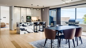 A modern kitchen with a marble island, bar stools, and a dining area with a table and chairs.