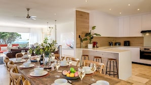 Une cuisine moderne avec des meubles blancs, un îlot central en bois et un coin repas doté d’une longue table pouvant accueillir six personnes.