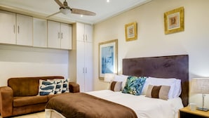 Une chambre à coucher avec un lit, un canapé marron, un ventilateur de plafond et une table de chevet.