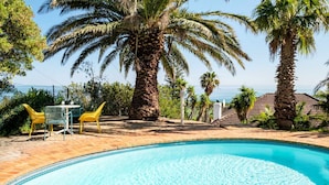 Une piscine à bord incurvé, entourée de palmiers et dotée d’une terrasse en briques.