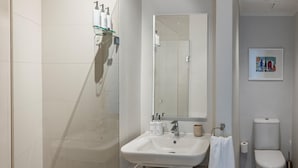 Une salle de bain avec un lavabo blanc, un miroir et des toilettes. Il y a un espace douche avec une porte en verre et une serviette accrochée au mur.