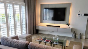 Un salon moderne avec un téléviseur à écran plat fixé au mur, une table basse en verre sur laquelle sont posés des magazines et un canapé.