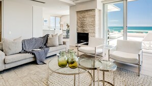 A modern living room with a sofa, chairs, a fireplace, and a view of the ocean. - Sapphire Tide Penthouse w Sea View Private Pool (Cape Town)