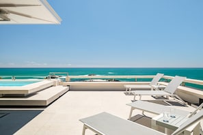 A rooftop terrace with a pool, lounge chairs, and a view of the ocean.