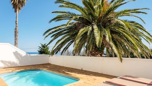 Une piscine entourée de chaises longues, de palmiers et d’un mur blanc.