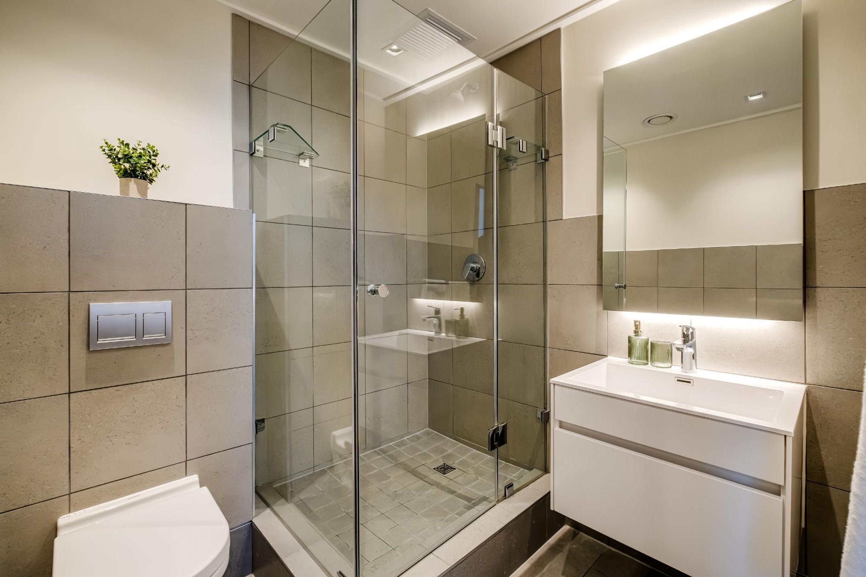 A modern bathroom with a glass-enclosed shower, a white sink, and a mirror above the sink.
