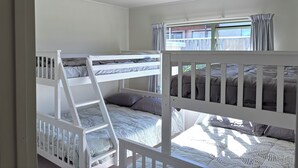 Una habitación con literas, una escalera, una ventana con cortinas y una lámpara en el techo.
