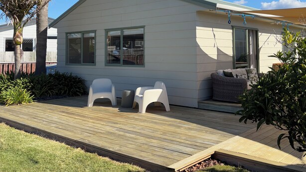 Una casa de un piso con una pequeña terraza, dos sillas de plástico blanco y un patio.