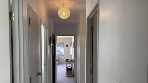 Un pasillo con paredes y puertas blancas que conduce a una habitación con ventana y una pequeña mesa.
