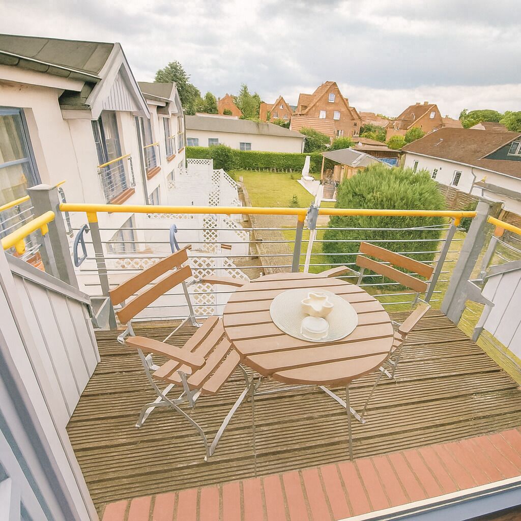 Ein Balkon mit rundem Tisch, Stühlen und einem gelben Geländer.